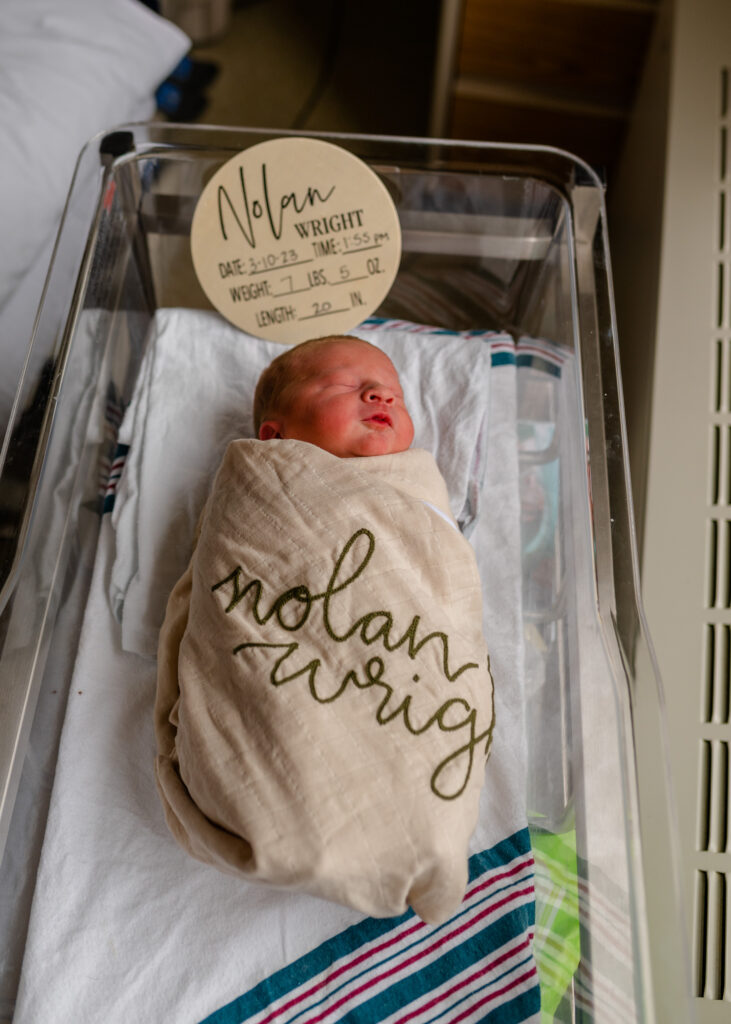 fresh 48 newborn in bassinet swaddled in blanket with newborn sign