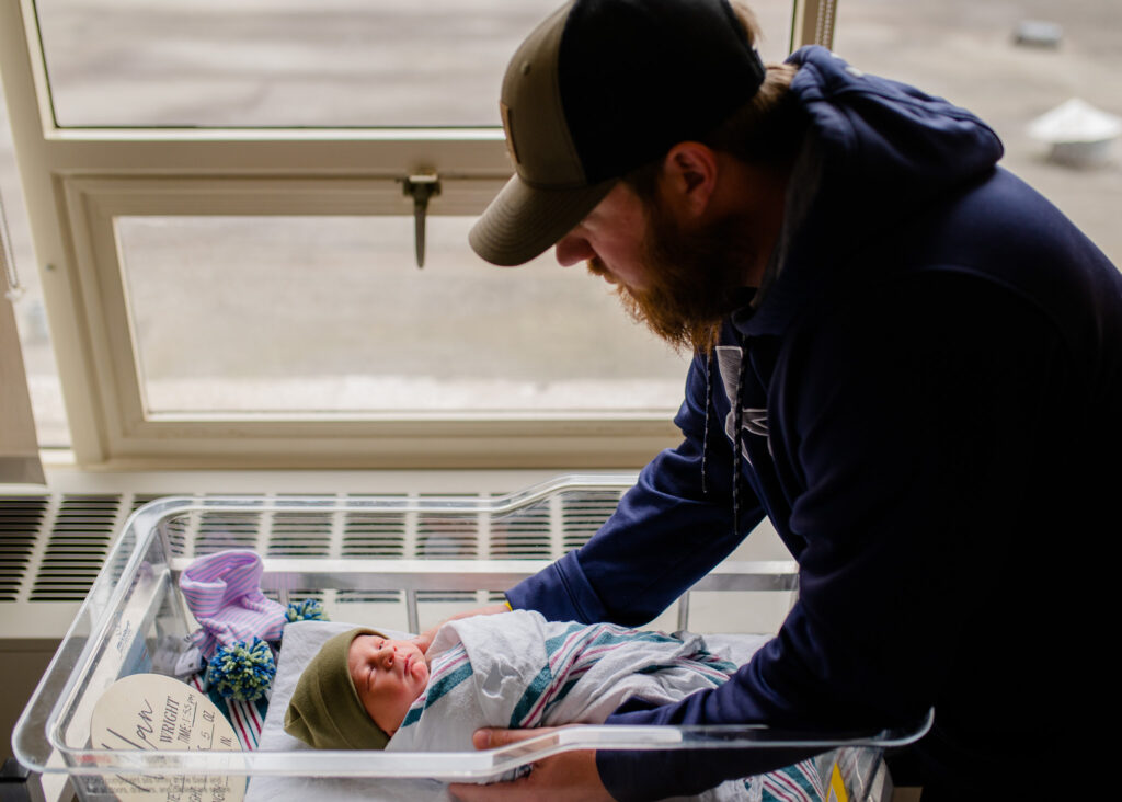 Dad looks at his newborn son in the bassinet in the hospital